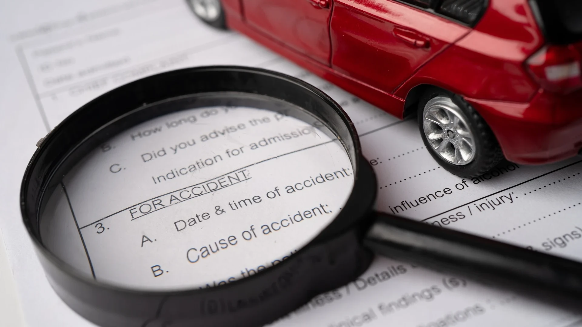 Model car with magnifying glass on top of a car accident claim form.